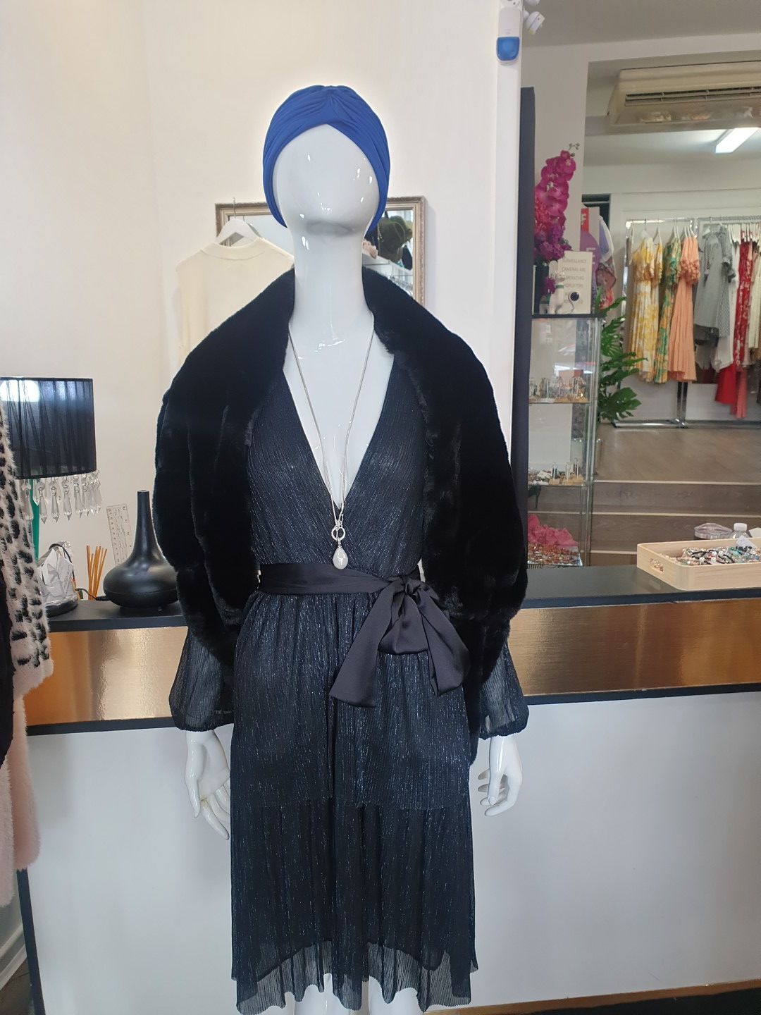 Mannequin in a black sparkly dress, faux fur jacket, blue turban, and necklace in a clothing store.