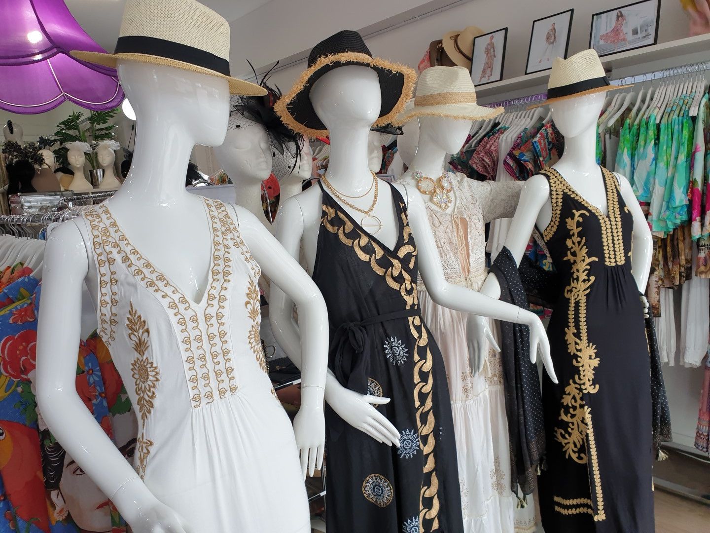Five mannequins wearing summer dresses and straw hats in a store setting.