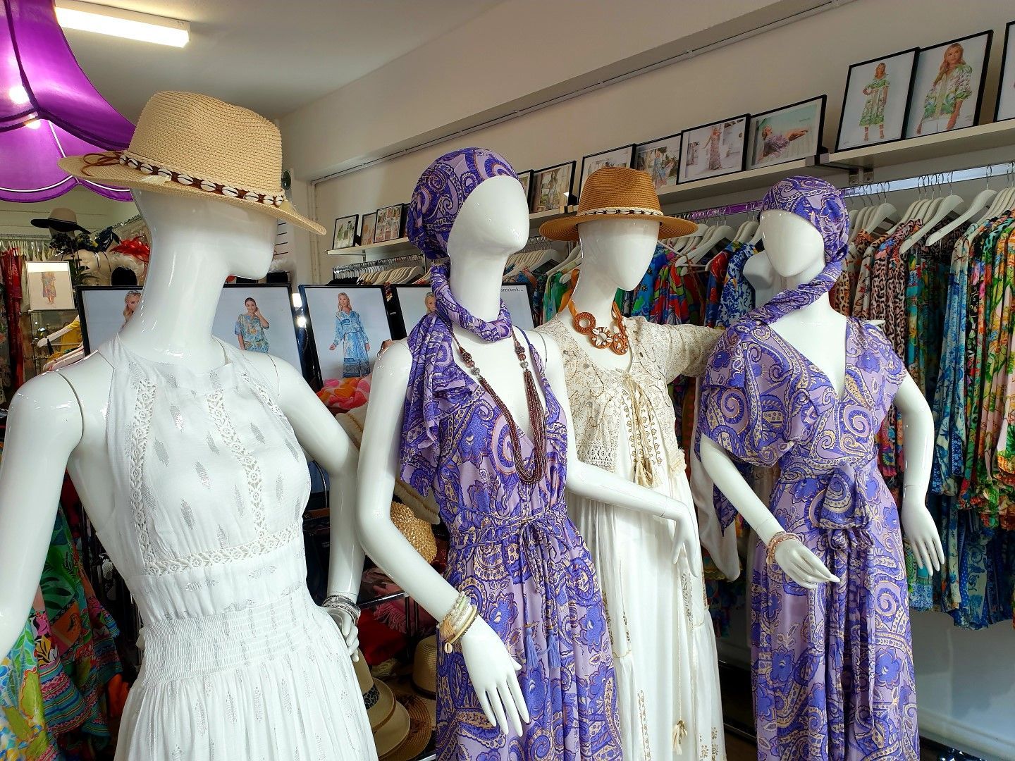 Four mannequins in a clothing store, wearing dresses and hats. Two purple dresses, one white dress, straw hats.