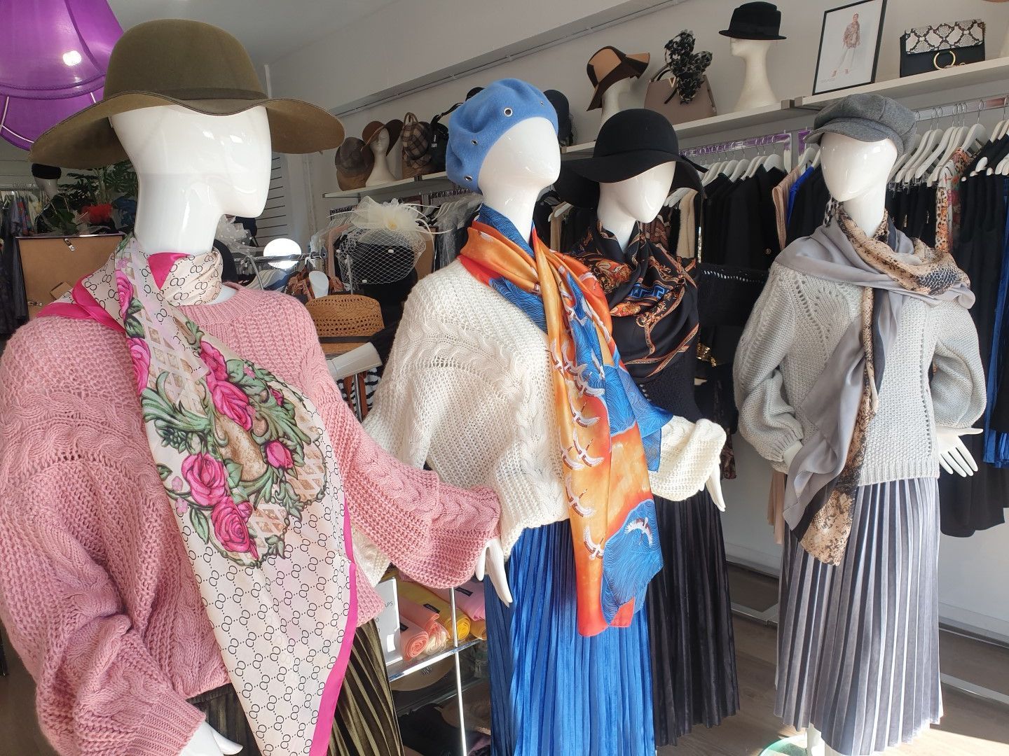 Clothing store window with mannequins wearing hats, scarves, sweaters, and skirts.