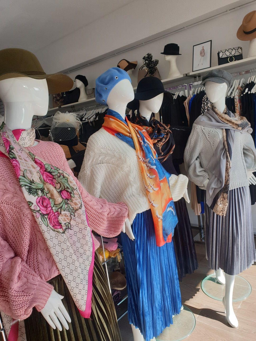 Mannequins in a shop wearing hats, scarves, and clothing. Sunlight fills the store.