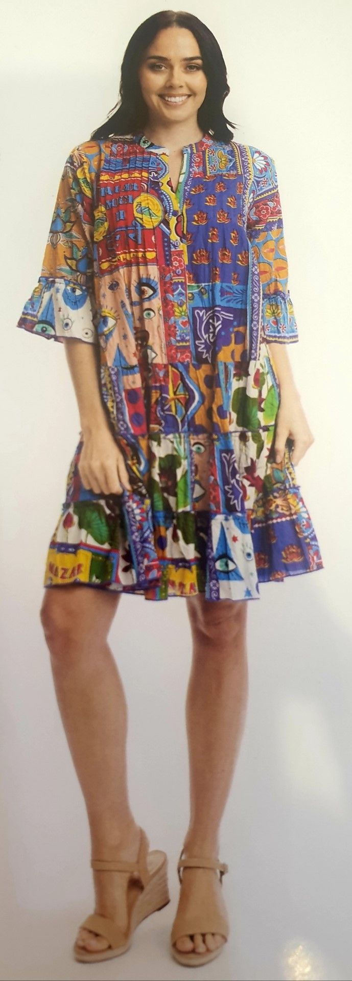 Woman in a colorful patterned dress smiles, wearing wedge sandals. White background.