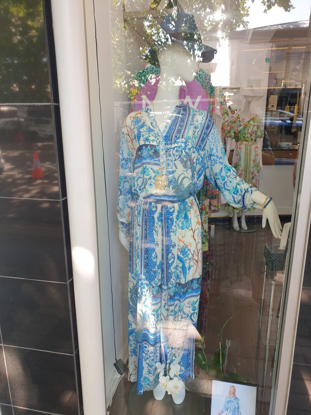 Mannequin in blue floral dress in a shop window. Sunlight reflects on the glass.