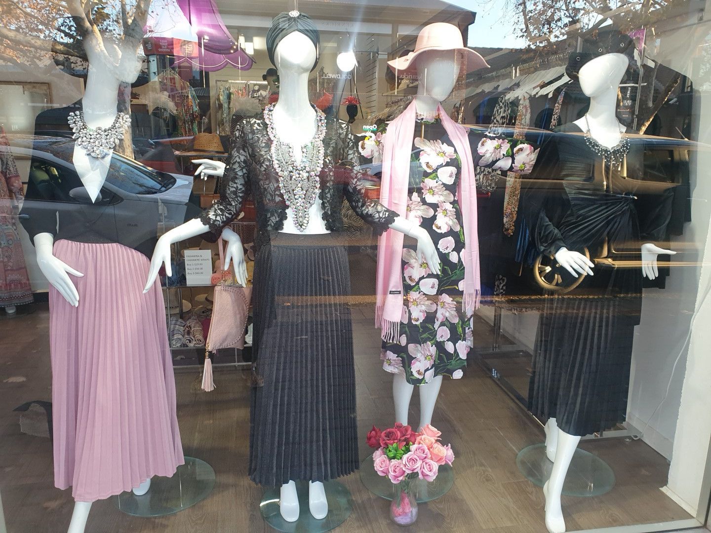Storefront display with four mannequins wearing vintage-style clothing, including dresses, skirts, and hats.