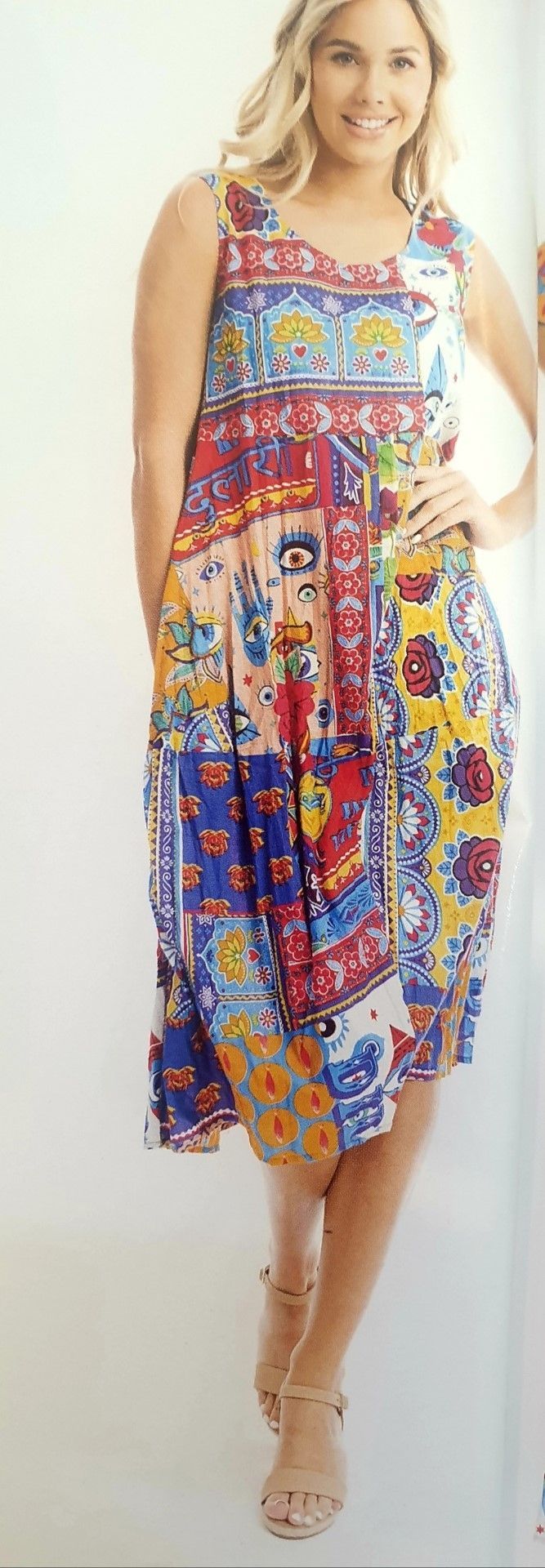 Woman in a colorful patchwork sundress and sandals smiles, posing in a bright setting.