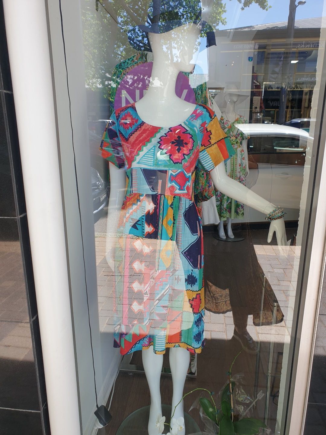 Mannequin in colorful patchwork dress and hat in store window.