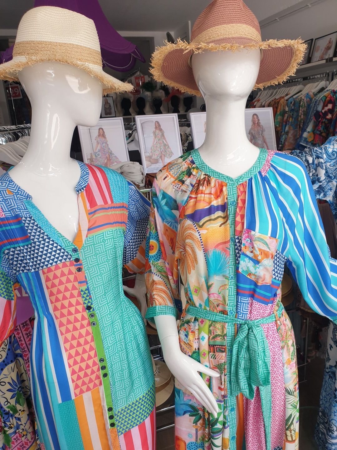Two mannequins wearing colorful summer dresses and straw hats in a store.