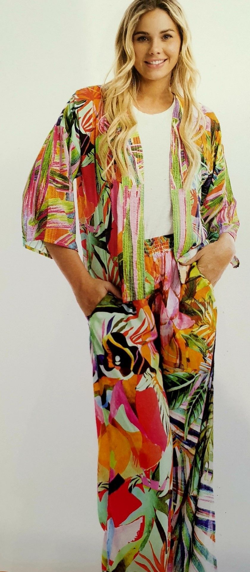 Woman in colorful floral print outfit smiling. White backdrop.
