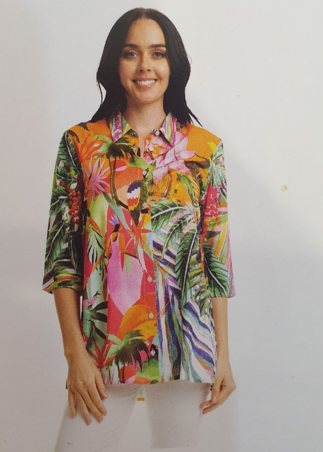 Woman wearing a vibrant tropical print blouse with white pants, smiling.