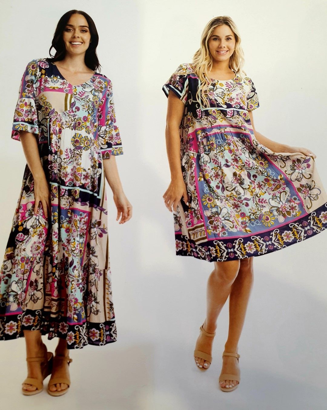 Two women wearing floral dresses, standing in a studio setting, smiling. One dress is long, the other short.