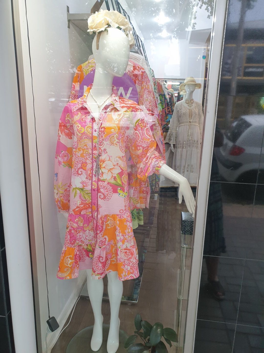 Mannequin in pink floral dress in shop window.