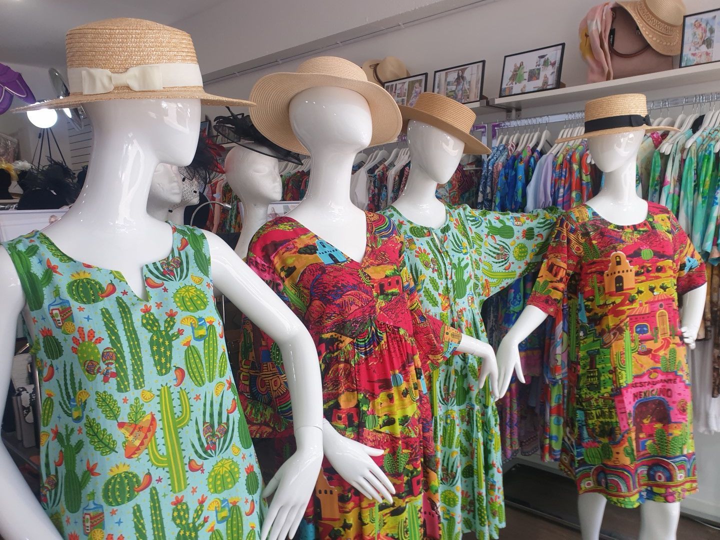 Mannequins wearing colorful summer dresses and straw hats in a clothing store.