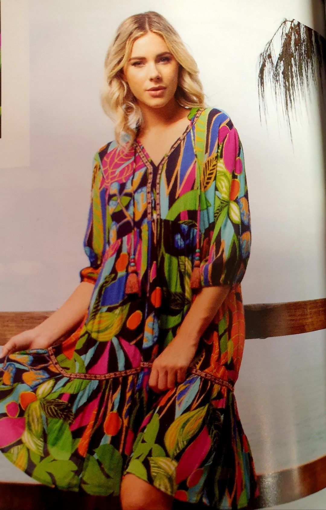 Woman in colorful floral dress, posing outside with blonde hair.