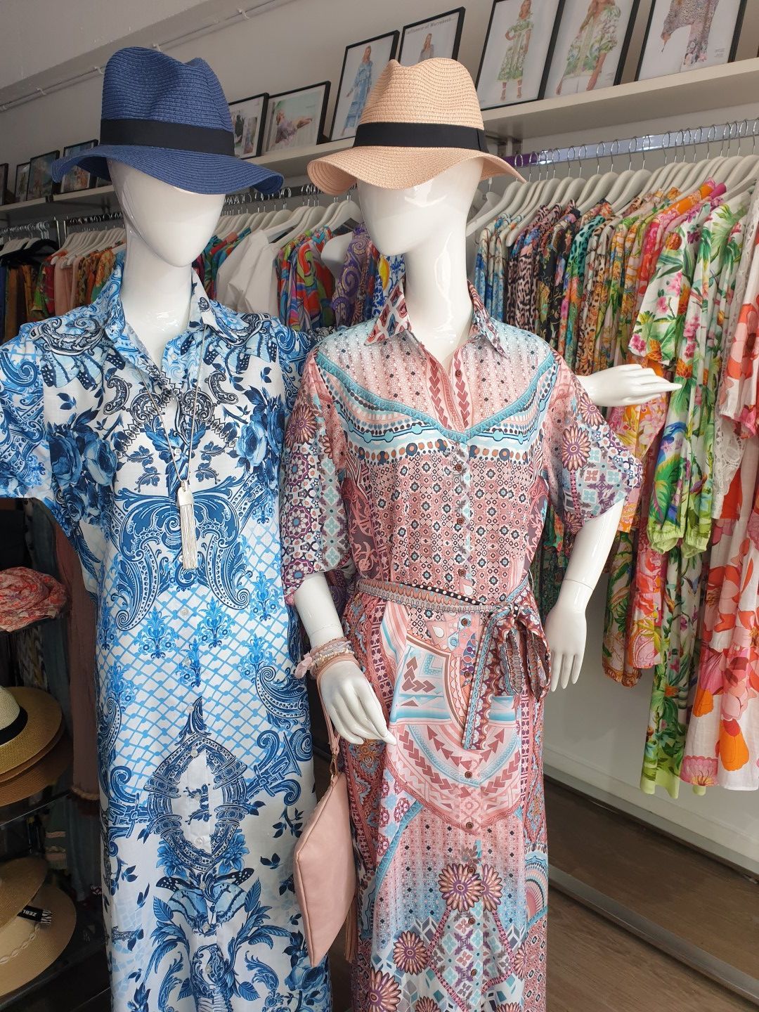 Two mannequins in dresses and hats in a clothing store. One blue dress, one pink dress.