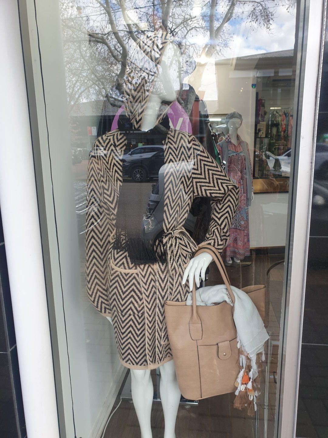 Mannequin in a window display wearing a beige and black patterned coat, holding a tan bag.