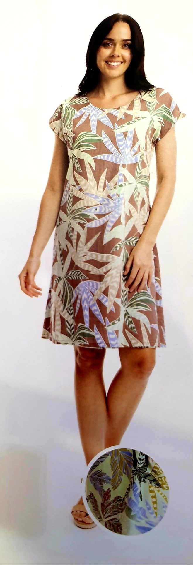 Woman in a floral dress smiles, standing on a white background. The dress has a brown leaf pattern.