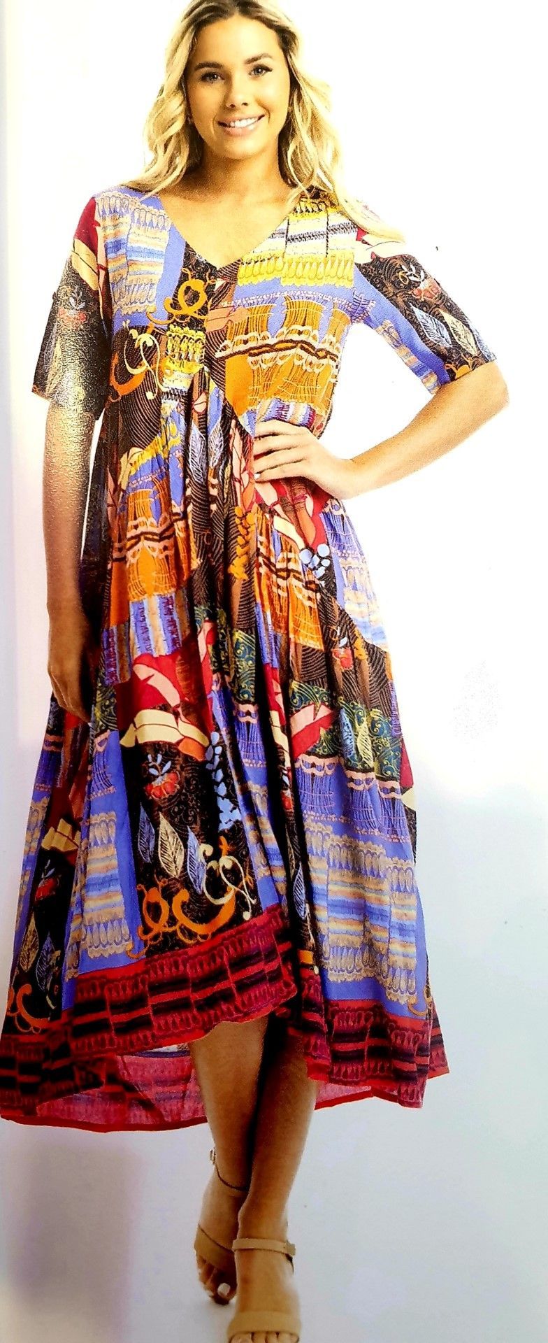 Woman in colorful print midi dress and sandals, smiling.