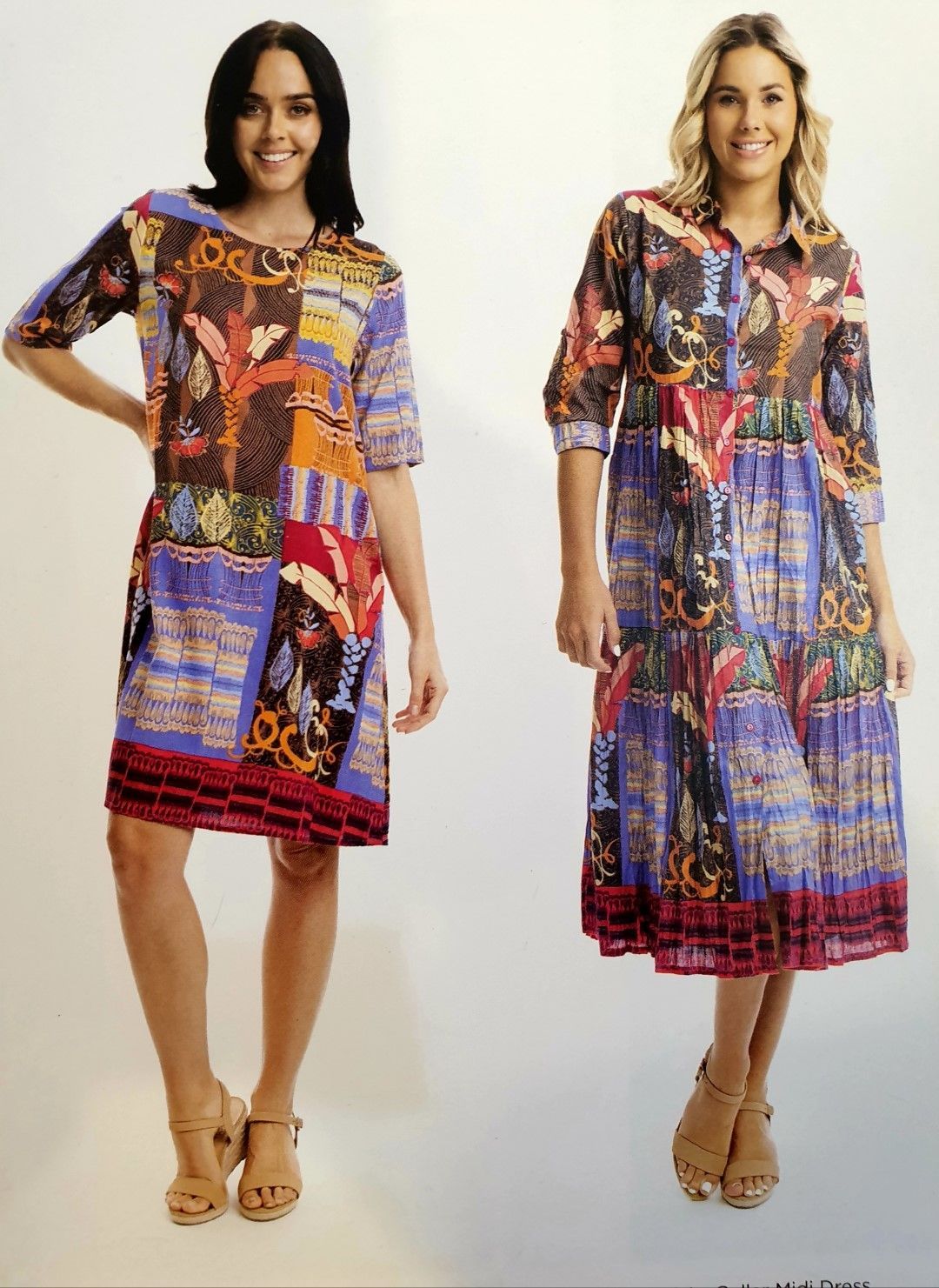 Two women modeling colorful patterned dresses, one wearing sandals, in a studio.