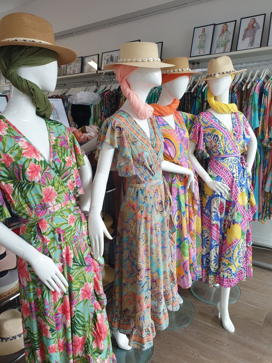 Mannequins in colorful floral dresses, hats, and scarves in a clothing store.