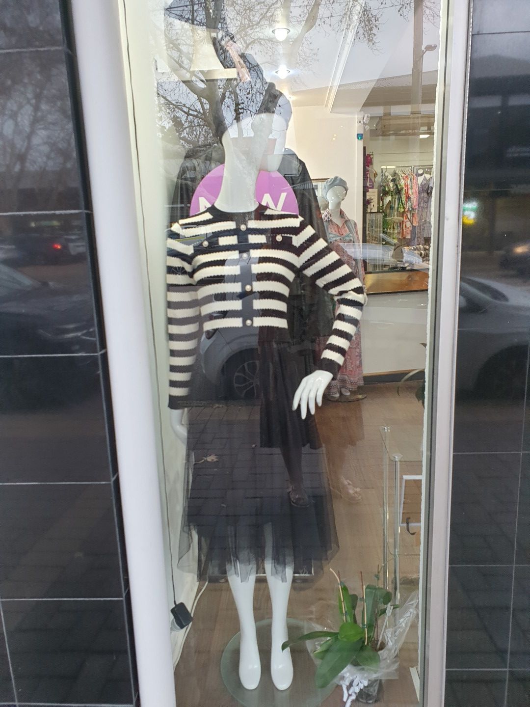 Mannequin in a storefront window, wearing striped sweater, black skirt, and hat.