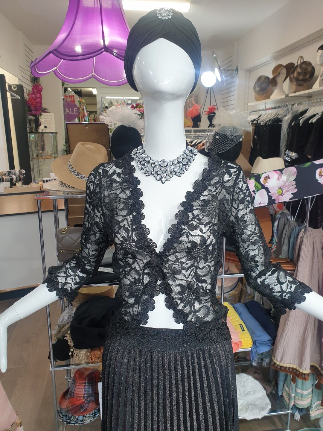 Mannequin in a shop window wearing black lace top, skirt, and necklace, black turban.