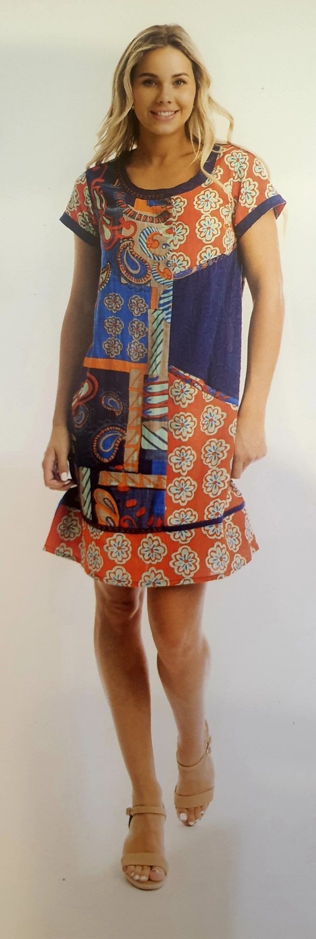 Woman in patterned dress and sandals poses in front of a white background.