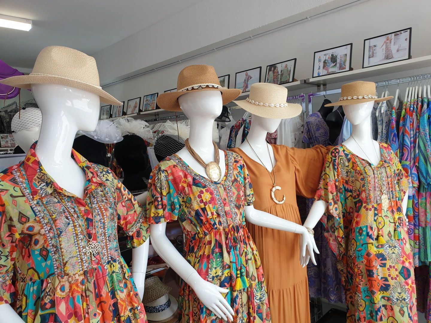 Four mannequins in a store display colorful summer dresses and straw hats.
