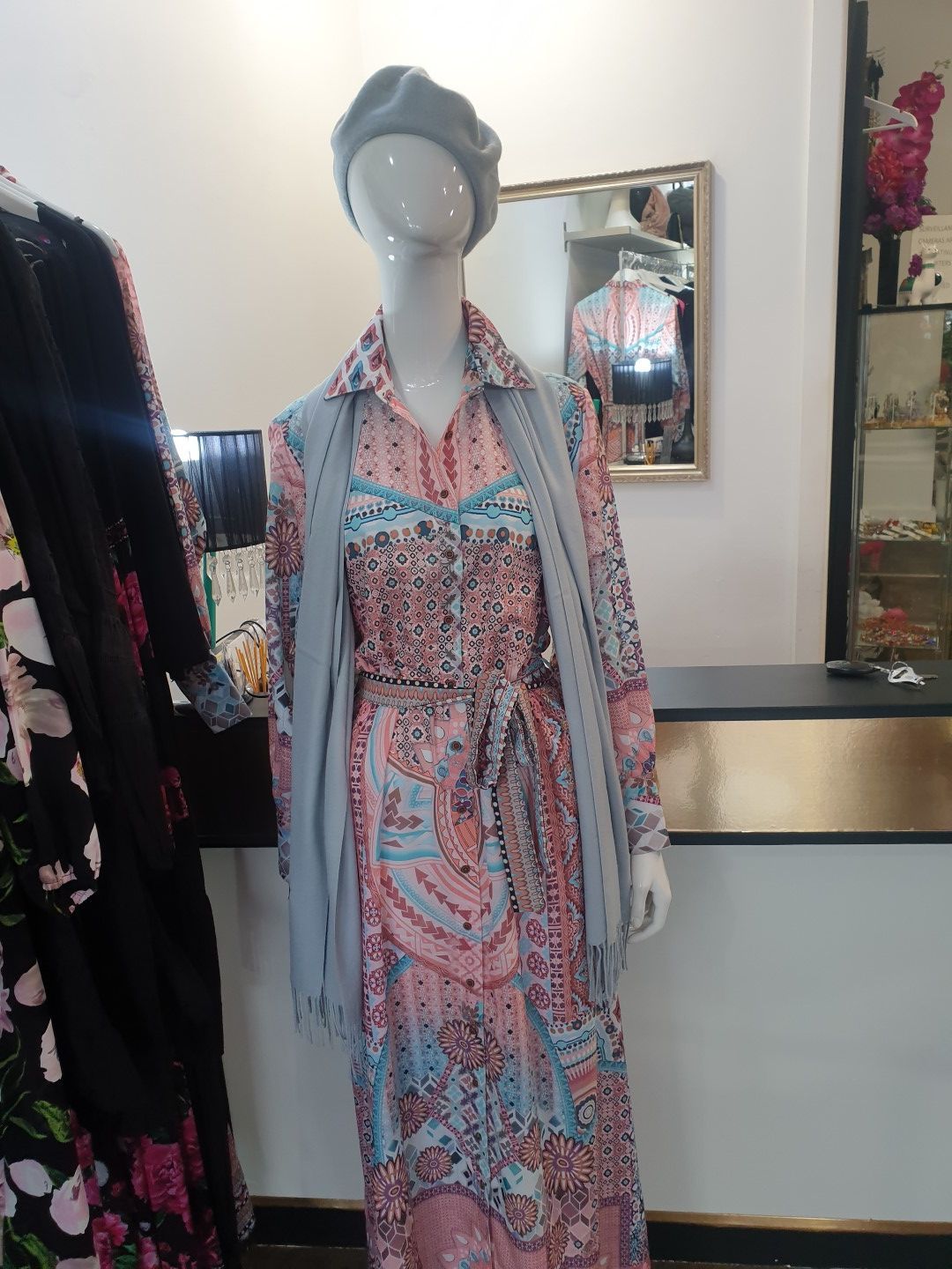 Mannequin wearing a patterned pink dress, grey scarf, and beret in a shop.
