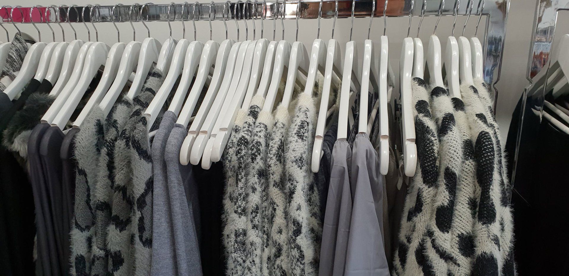Clothes hanging on white hangers on a metal rack; mostly gray and black sweaters.