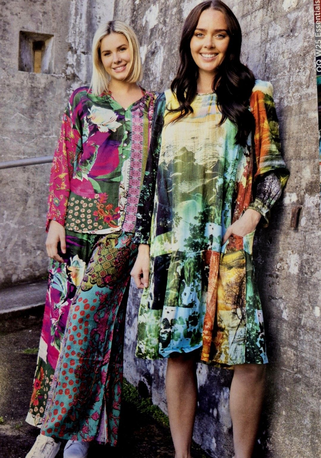 Two women in colorful patterned clothing standing outdoors near a weathered wall.