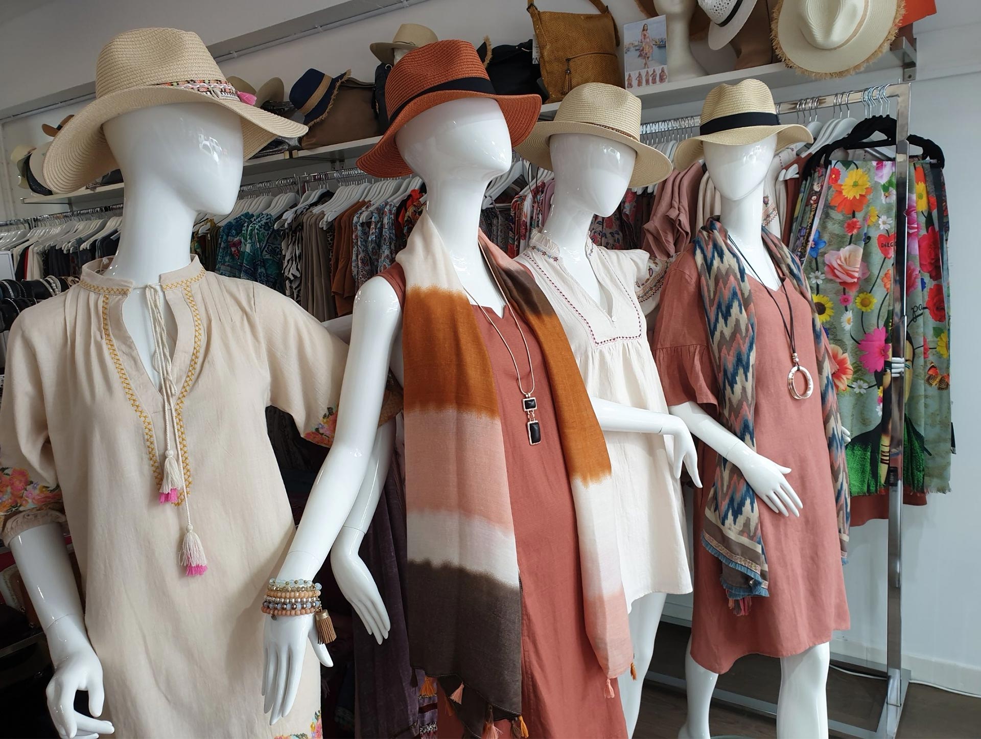 Four mannequins wearing summer clothing and hats in a clothing store.