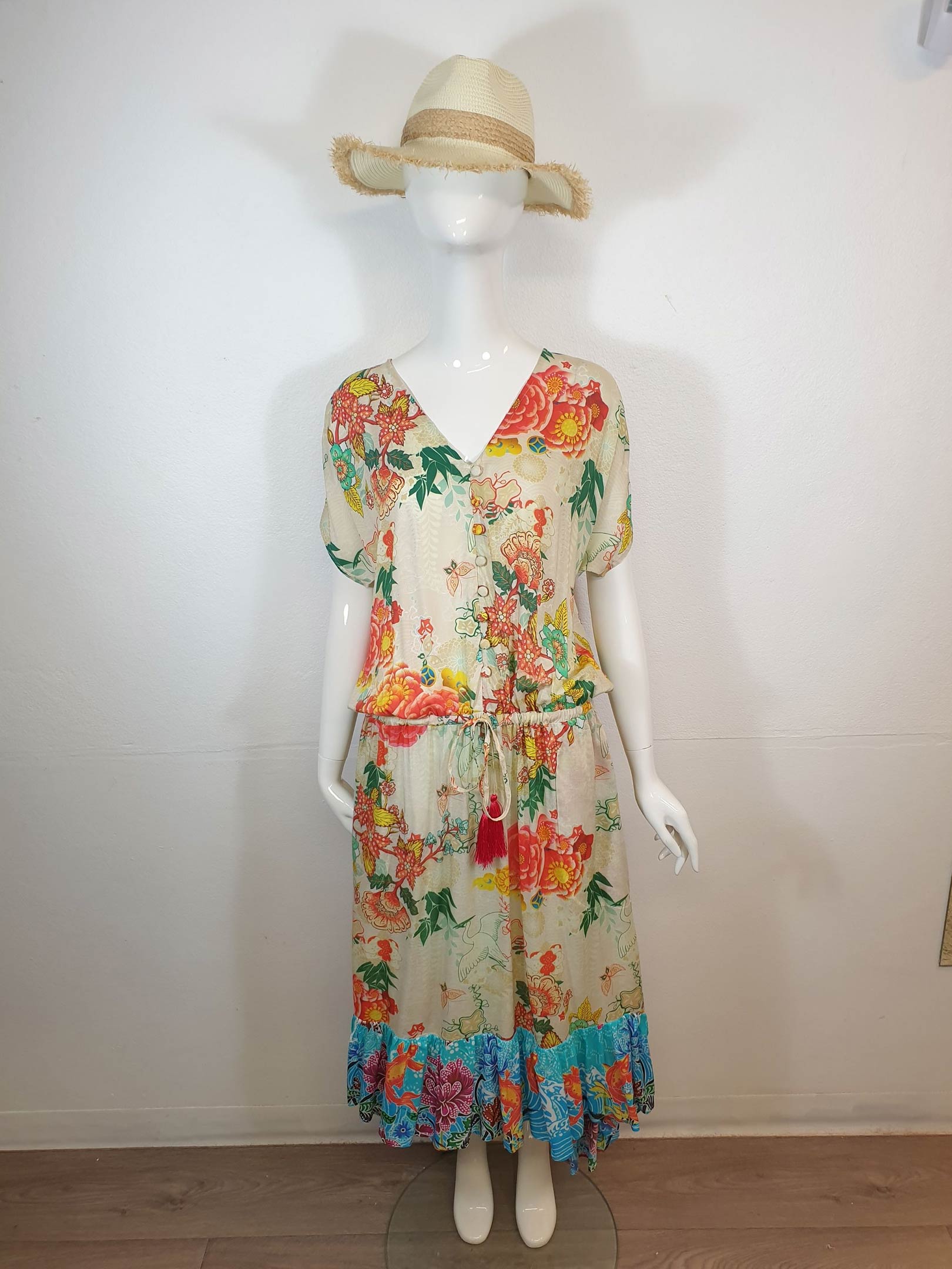 Mannequin wearing a floral print dress with a straw hat. Dress has a blue and teal hem.