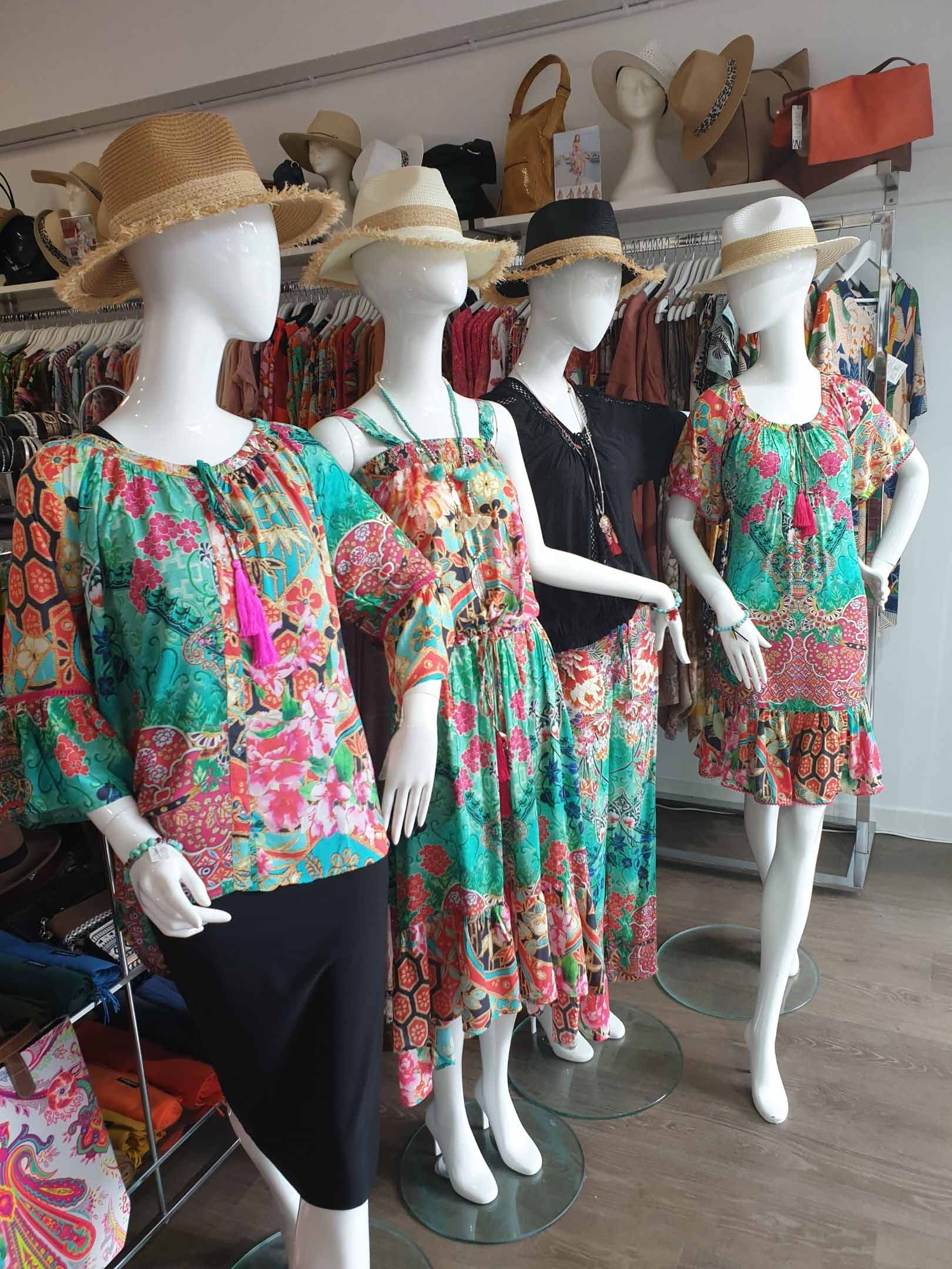 Four mannequins wearing floral dresses and straw hats in a boutique.