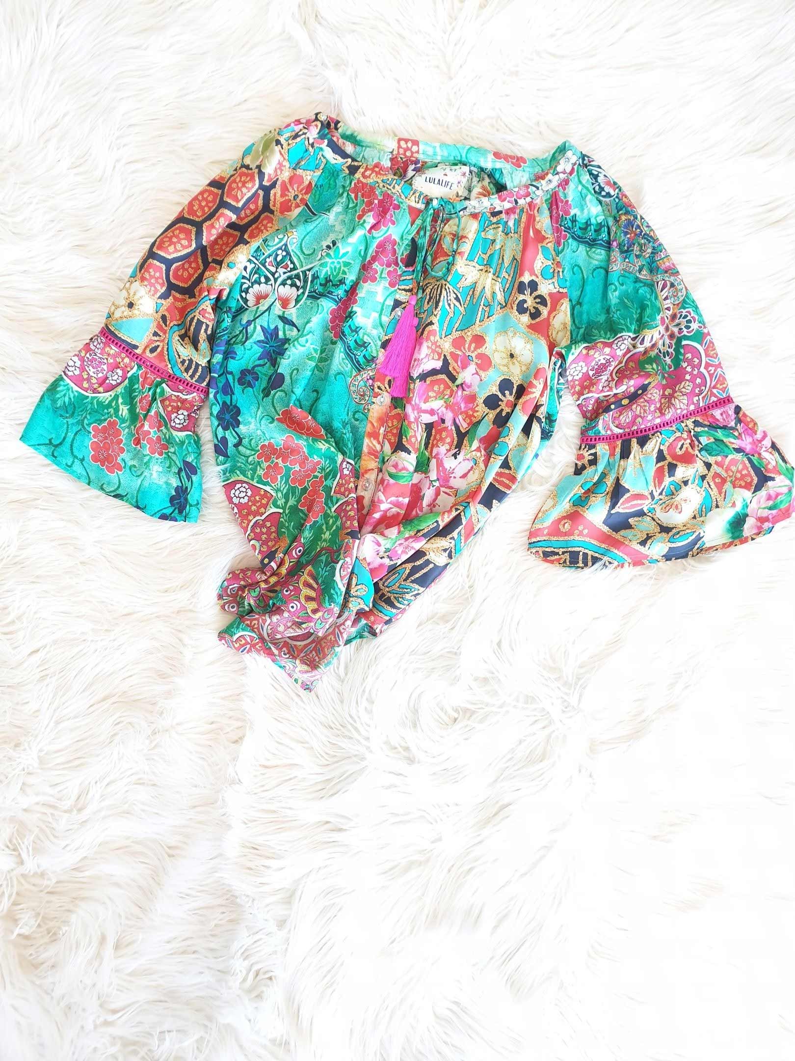 Colorful floral blouse with bell sleeves on a white fur background.