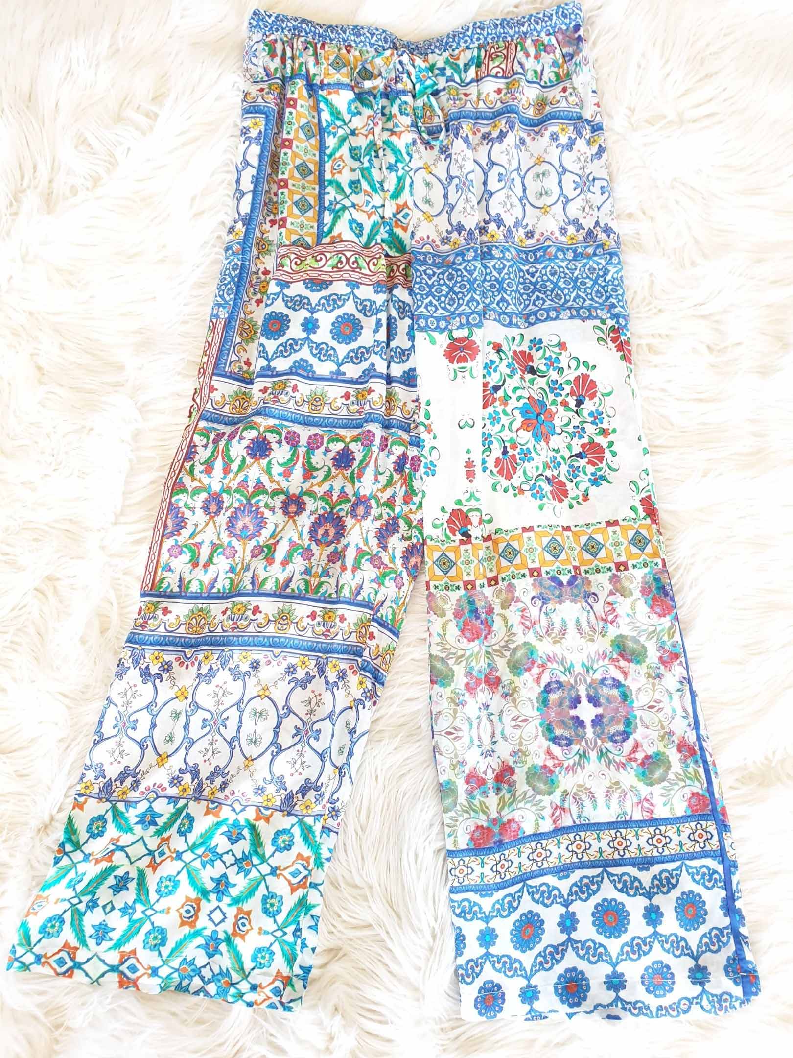 Patchwork print pants with floral and geometric designs in blue, white, and teal on a fluffy surface.