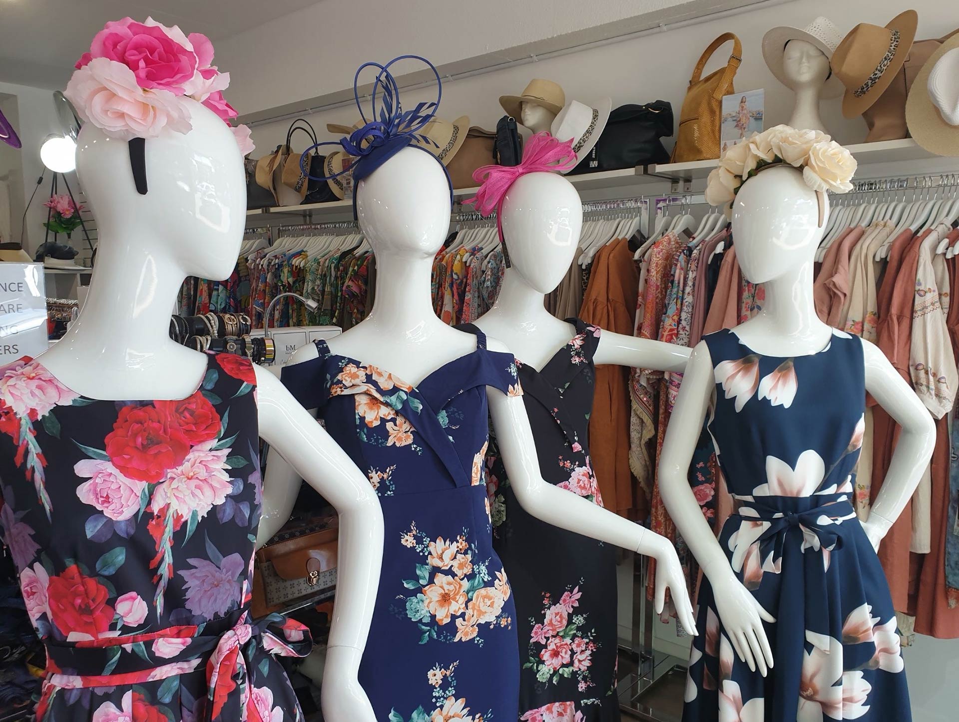 Four mannequins wearing floral dresses with hats in a clothing store.