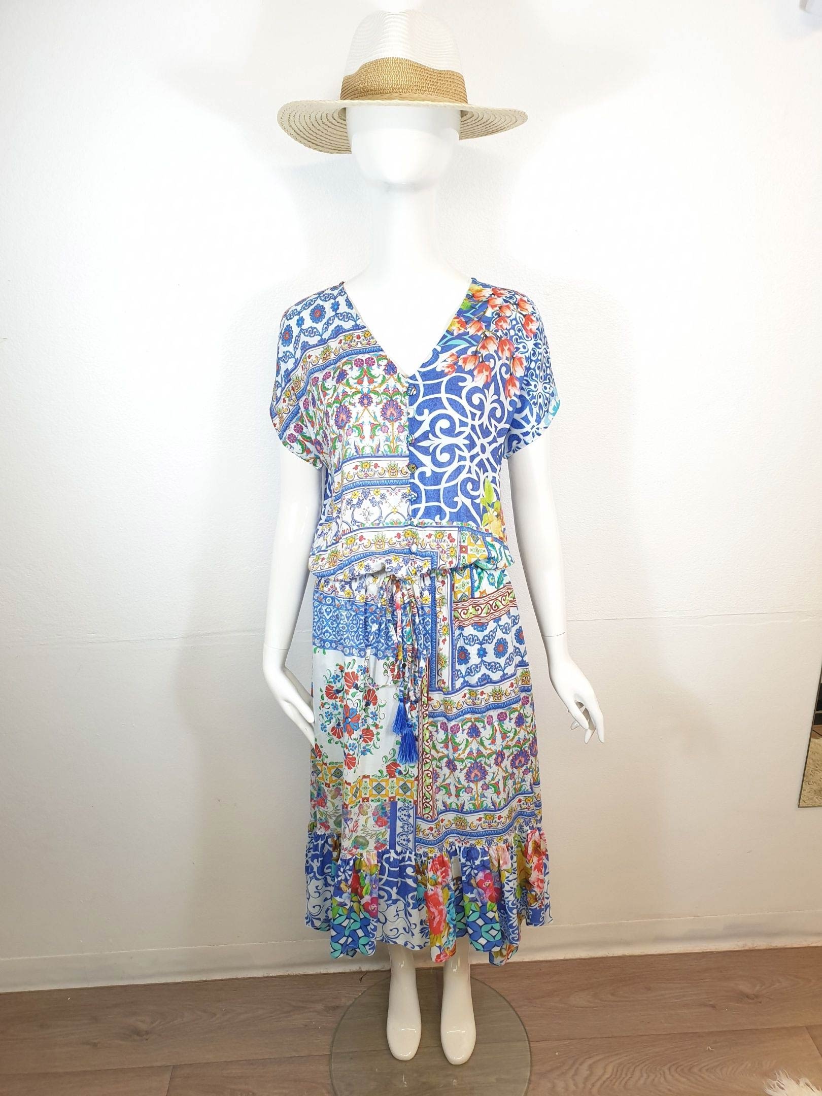 Mannequin wearing a blue patterned midi dress and straw hat indoors, against a white wall.
