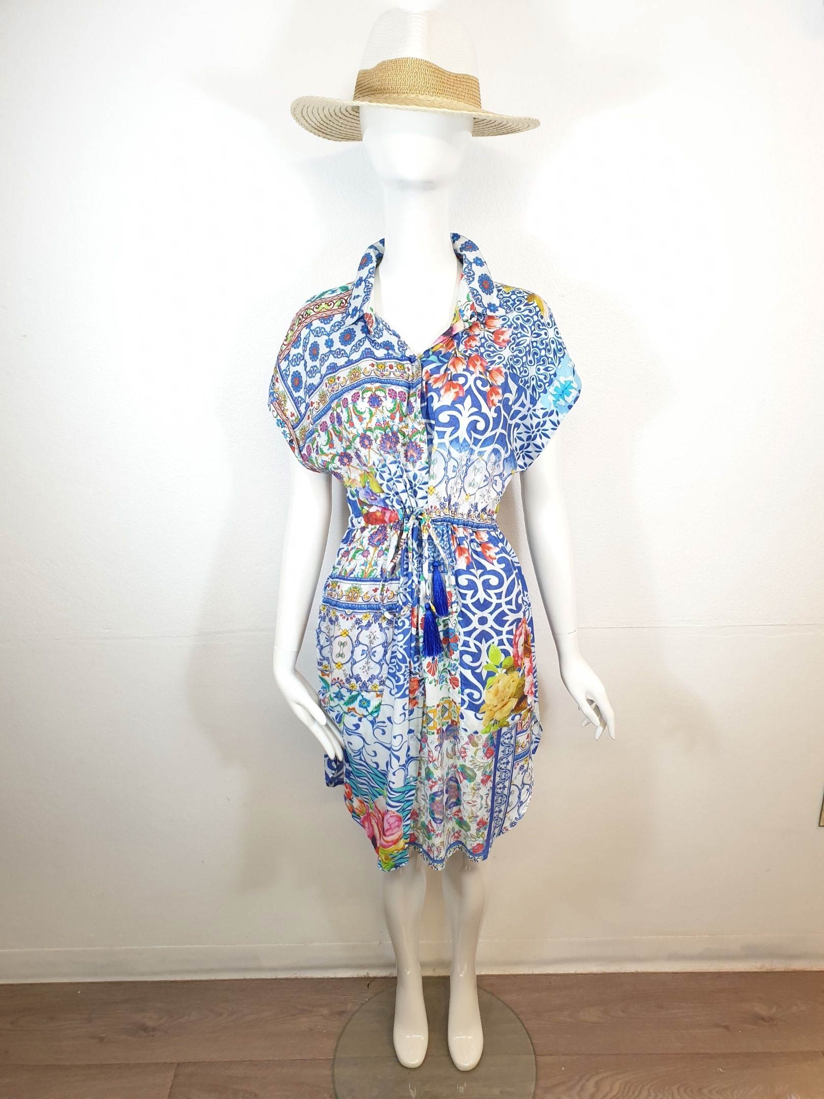 Mannequin wearing a blue, white, and floral-patterned dress, cinched at the waist, with a straw hat on its head.
