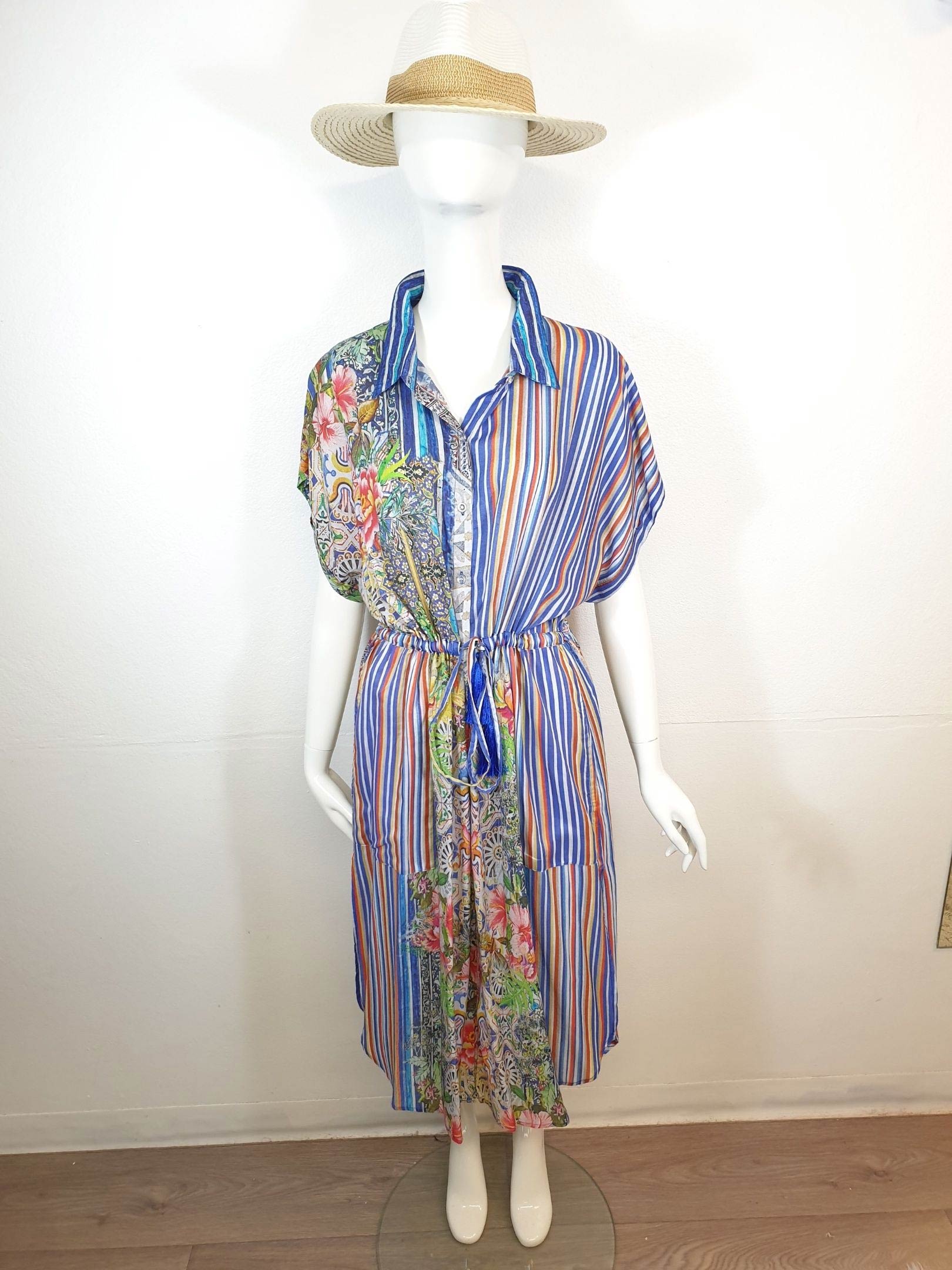 Mannequin wearing a colorful, patterned shirt dress and straw hat, indoors.