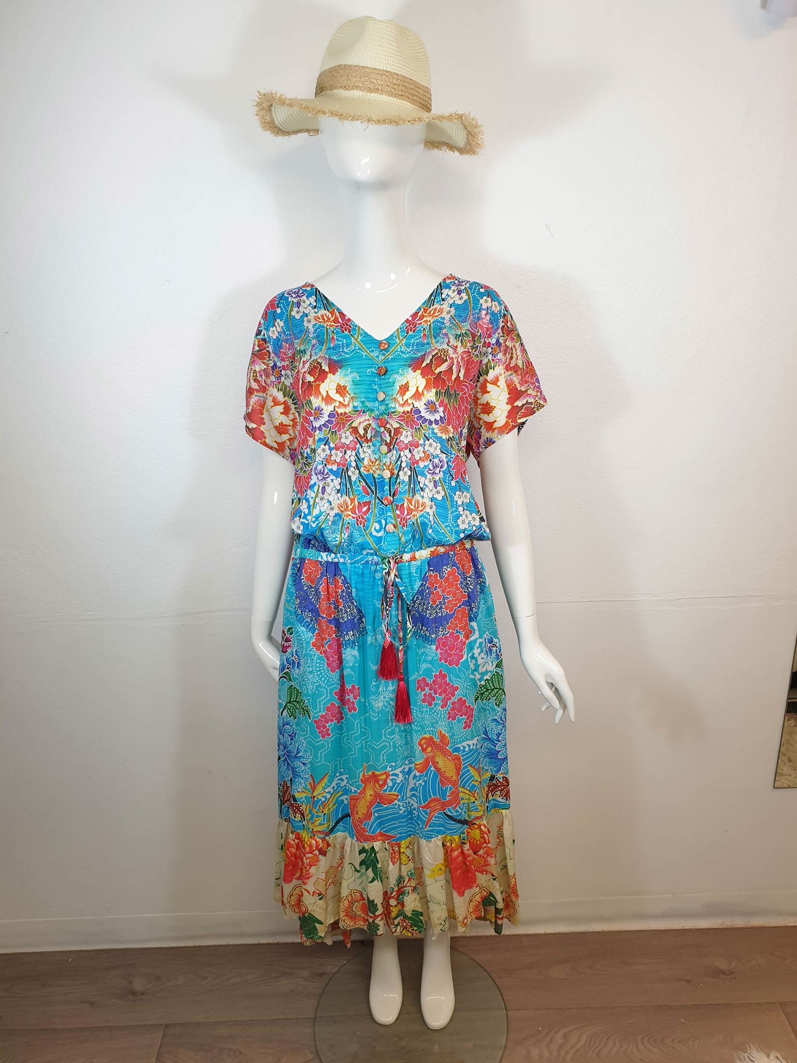 Mannequin wearing a floral print dress and straw hat, with a blue waist tie.