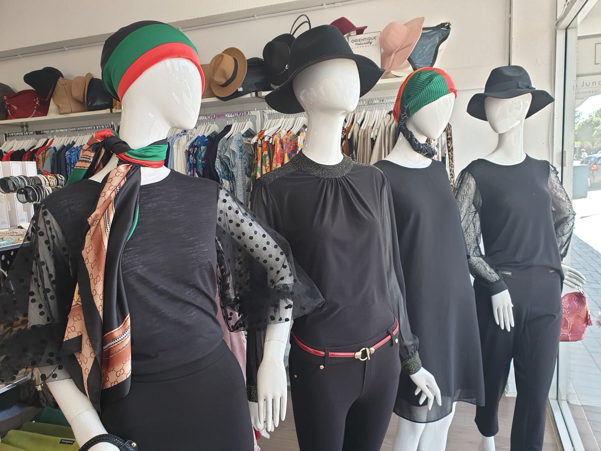 Mannequins in a shop window display, wearing black outfits and hats.