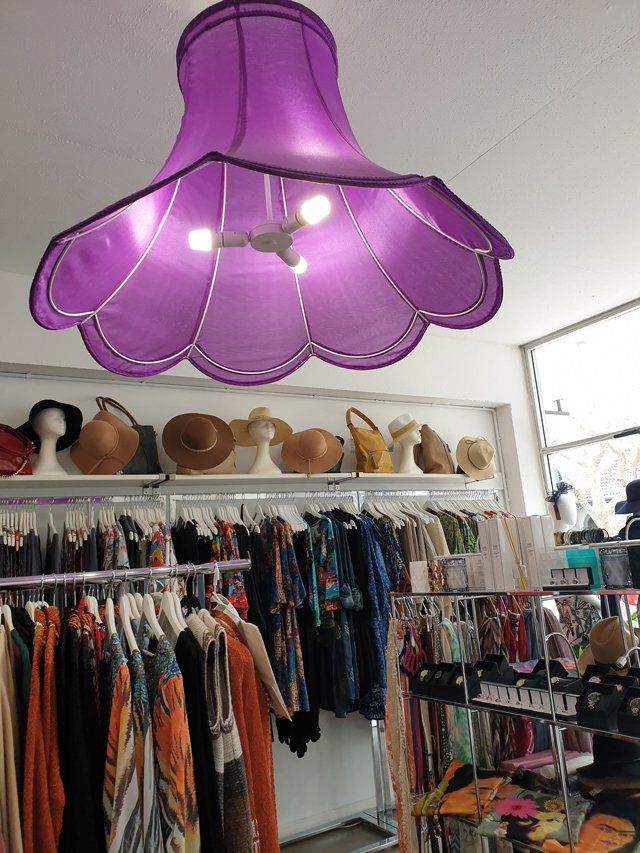 Purple flower-shaped lamp hanging above a vintage clothing store with racks of clothes and hats.