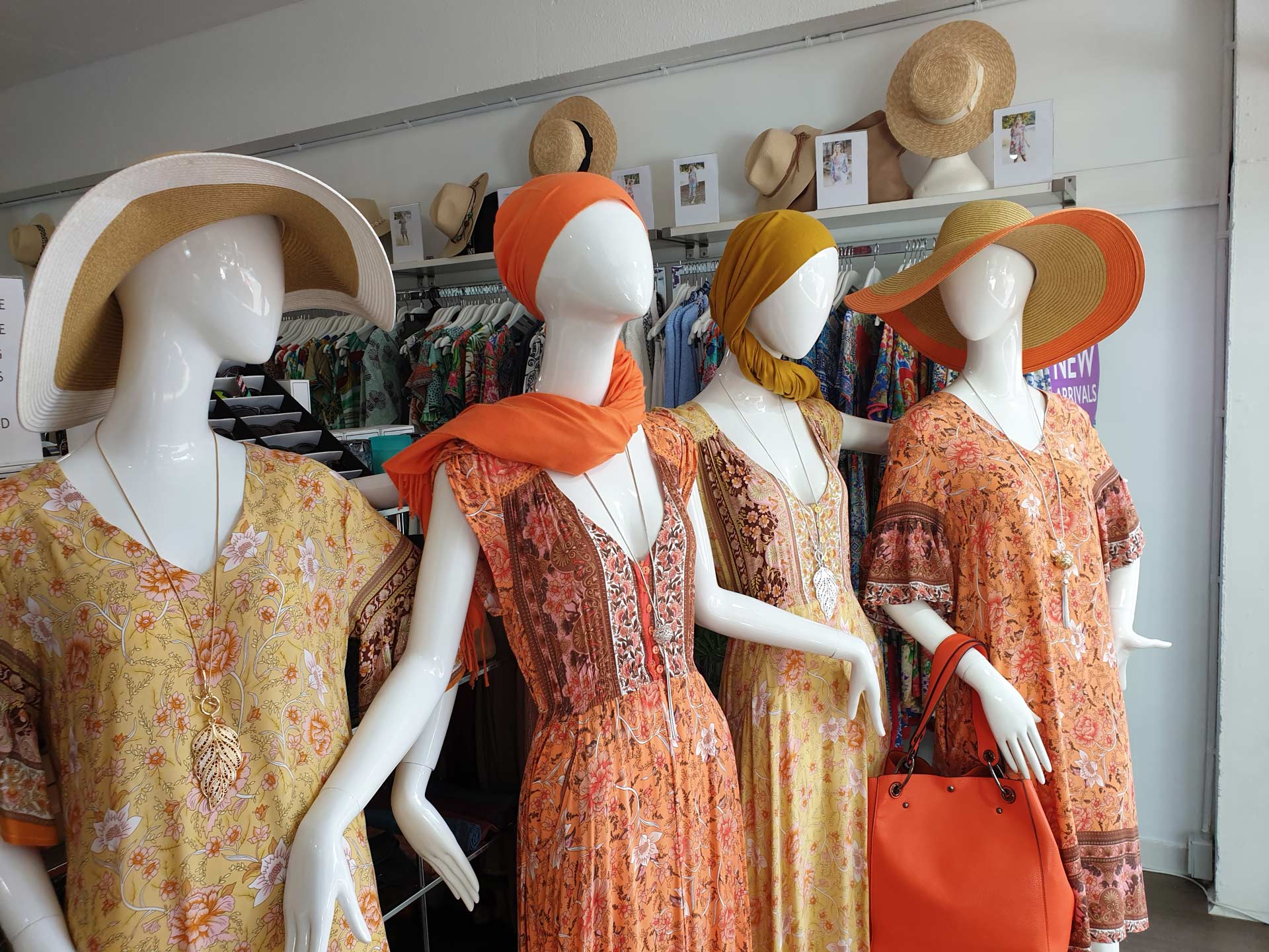 Four mannequins in an orange/yellow dress, hat, scarf, and purse. A retail clothing store.