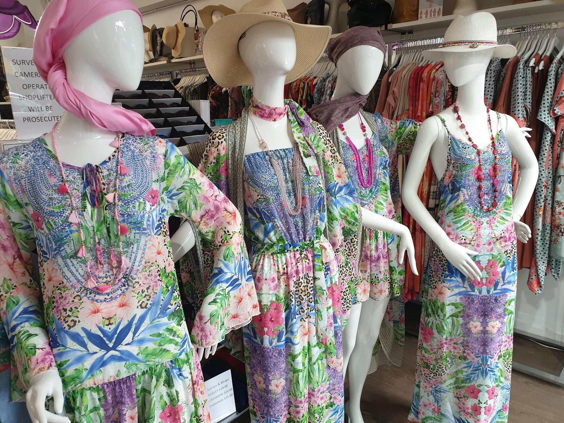 Four mannequins in a store display floral dresses and accessories.