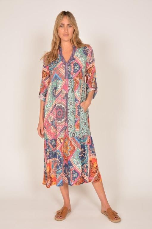 Woman in a colorful patterned midi dress and sandals, posing against a white background.