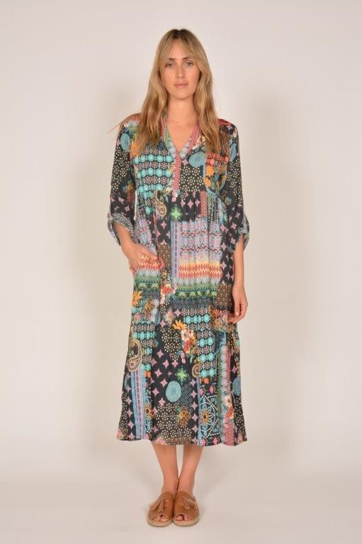 Woman in a colorful patchwork dress, standing in front of a white backdrop, wearing sandals.