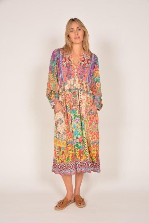 Woman wearing a colorful floral dress with pockets, standing against a white backdrop.