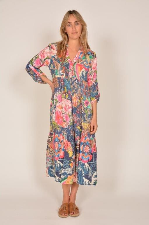 Woman in a colorful floral midi dress stands facing forward, hand on hip, in a studio setting.