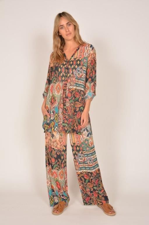 Woman in a patterned floral tunic and wide-leg pants; standing against a white backdrop.