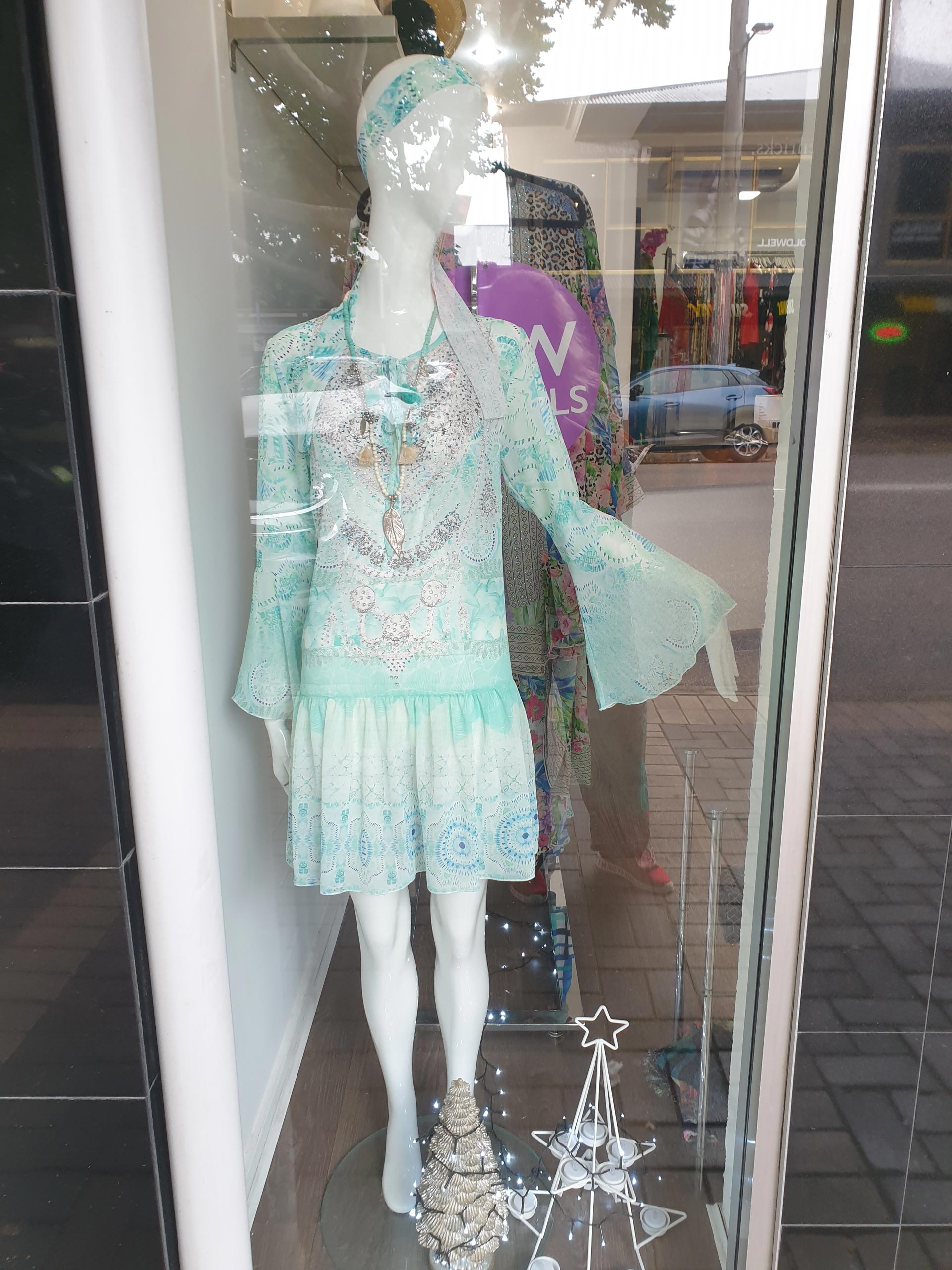 Mannequin in a boutique window wearing a turquoise dress and a matching head wrap.